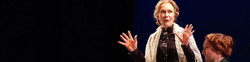 A woman wearing a shawl grins and holds out her hands excitedly. 