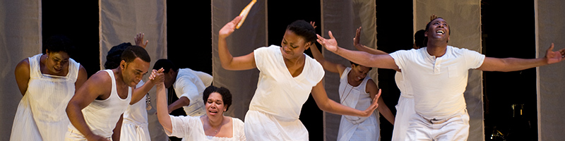 A group of people wearing white sing and dance onstage.