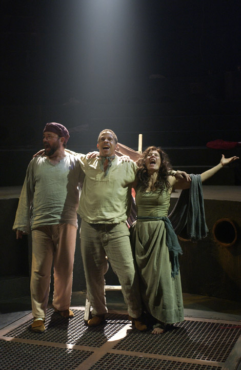 A group of three people stand with their arms around one another. They appear to be shouting or singing.