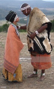 A man and a woman stand facing one another wearing traditional Xhosa garb.
