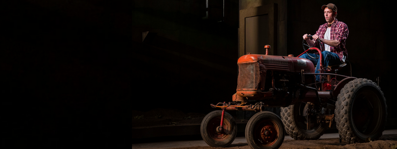 A man rides a large, red tractor on a black stage.