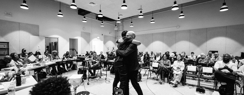 Two men embrace in a crowded room.