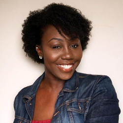 A woman wearing a denim jacket smiles at the camera. Her body is at a slight angle to the camera.