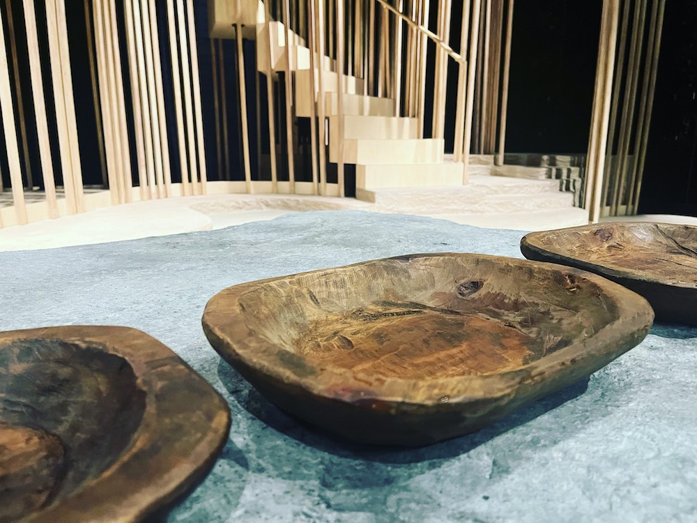 Three hand-carved wooden bowls next to one another on an empty stage.