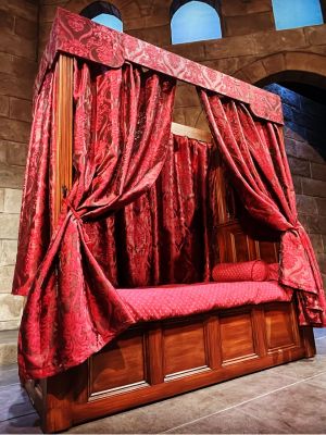 A four-poster wooden bed with red upolstery.