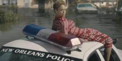 A still from Beyonce's "Formation" music video shows the singer laying on top of a New Orleans police car amidst a flooded street.