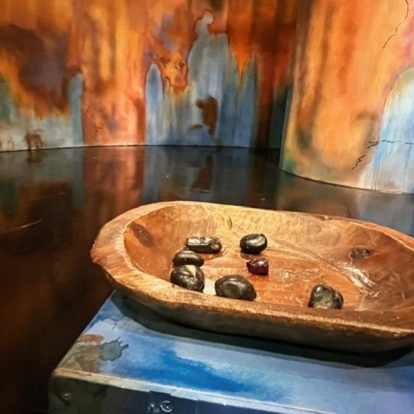 A wooden bowl filled with stones rests on stage. There is a colorful wall behind the bowl.