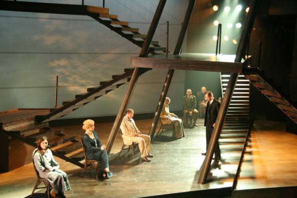 A row of people sitting in chairs under an interlocking set of stiarcases.