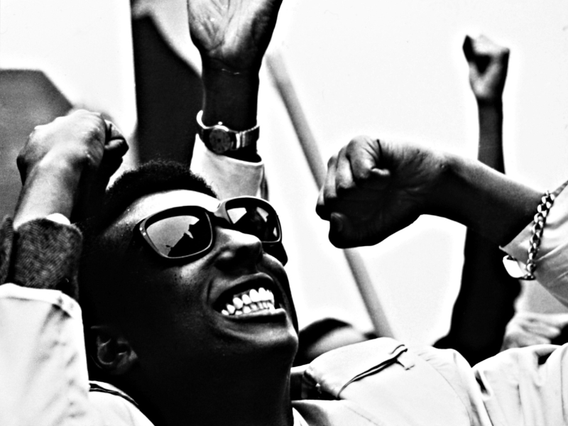 A smiling man in sunglasses makes a celebratory motion.