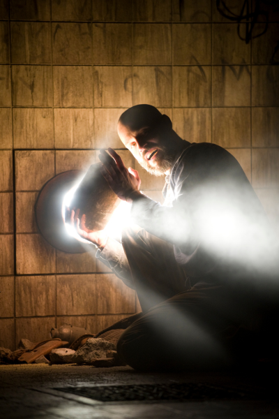 A crouching man holds an object up to a small window.