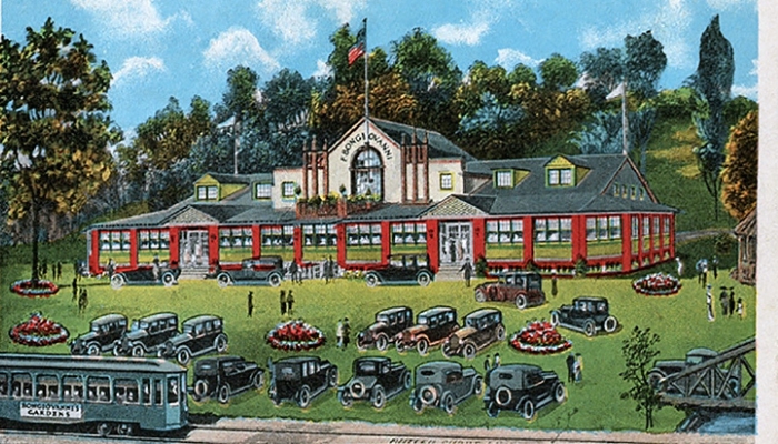 An illustration of a resort house. There are several cars parked on the front lawn in two rows, with several more lined up by the door. The resort is two stories with an American flag at the top. Trees surround the building.