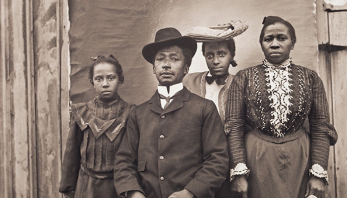 A Black family from Worcester, Massachusetts, poses for a photograph. The father sits, while the mother and two daughters stand.