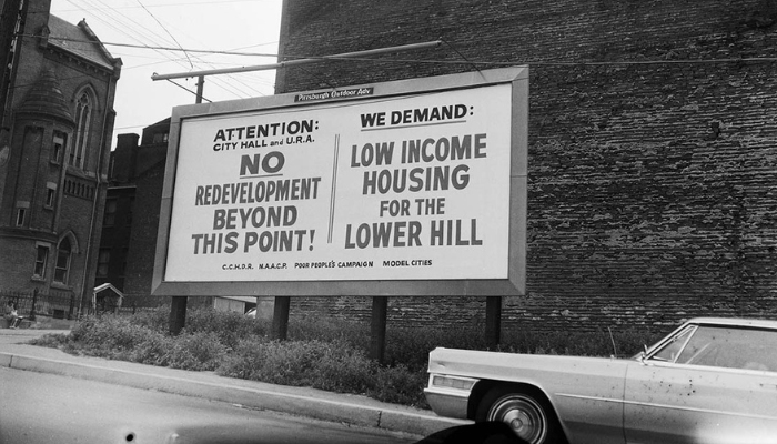 A billboard divided into two side-by-side sections. The left one reads: “Attention City Hall and URA: NO Redevelopment Beyond this Point.” The right side reads: “Low Income Housing for the Lower Hill.”