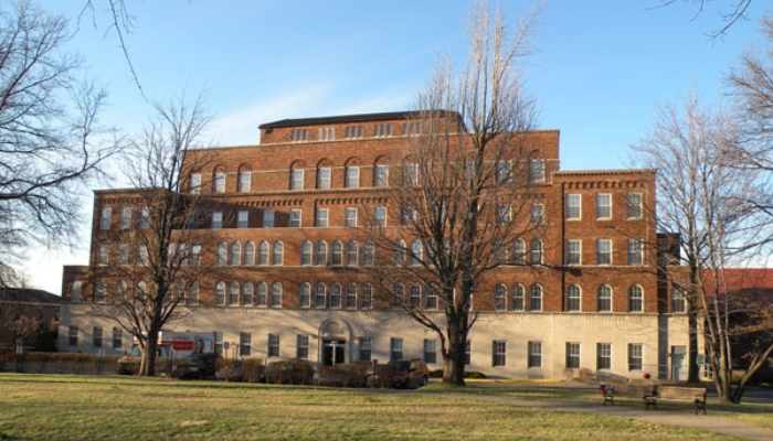 A large brick building with bare trees in front of it, photographed in color.