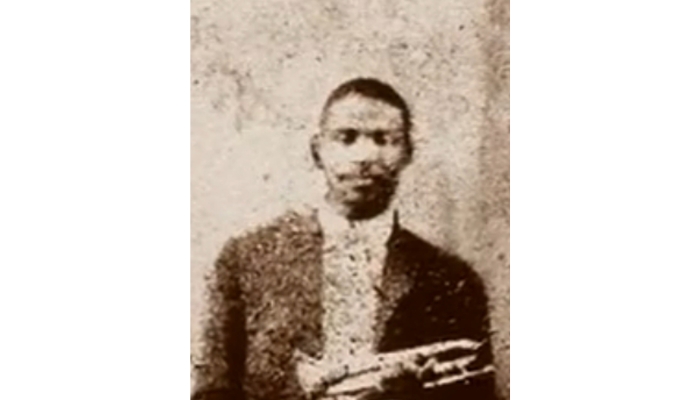 A fuzzy photograph of Buddy Bolden wearing a suit and holding his coronet.