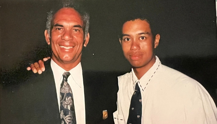 A young Tiger Woods with his arm around an older Black gentleman who is grinning and has salt-and-pepper hair.