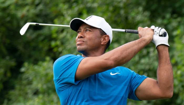 Tiger Woods gazes into the distance as he holds the end of his swing. He wears a blue golf shirt, white hat, and one white glove.